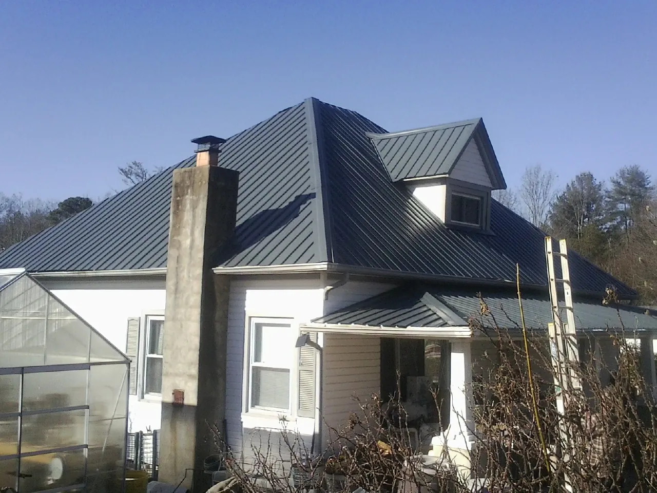 Dark blue standing seam metal roof on a white farmhouse with dormer — Slate & Tile Roof Repair by Roofing Brothers in Newalla