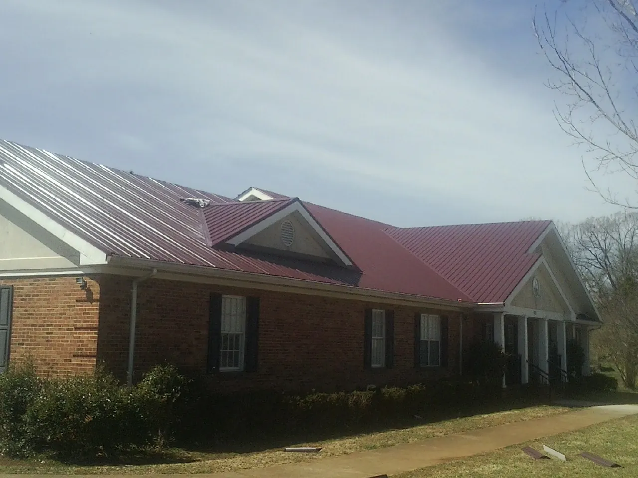 Red metal roof with gabled entries on a long brick building, from a Hail Damage Roof Repair job in Newalla