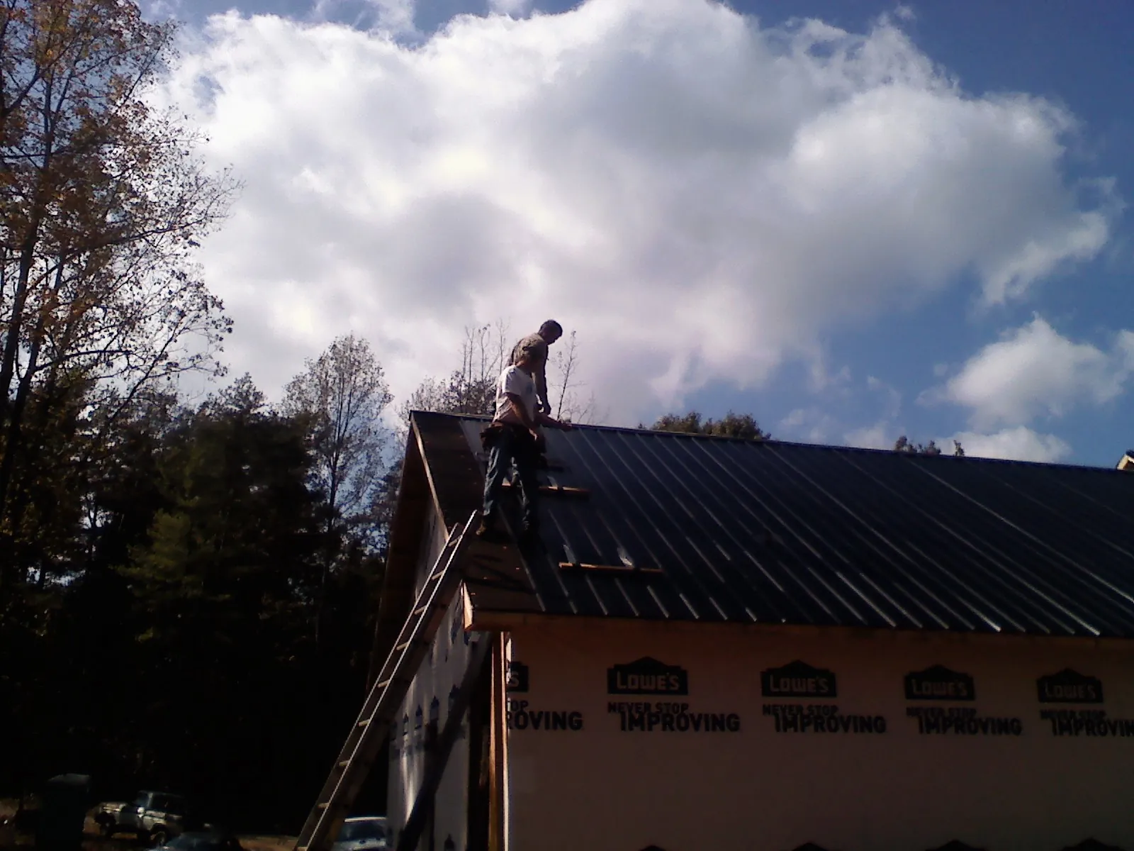 Roofer fastening dark metal panels high against a cloudy sky, from a Roof Inspection job in Newalla