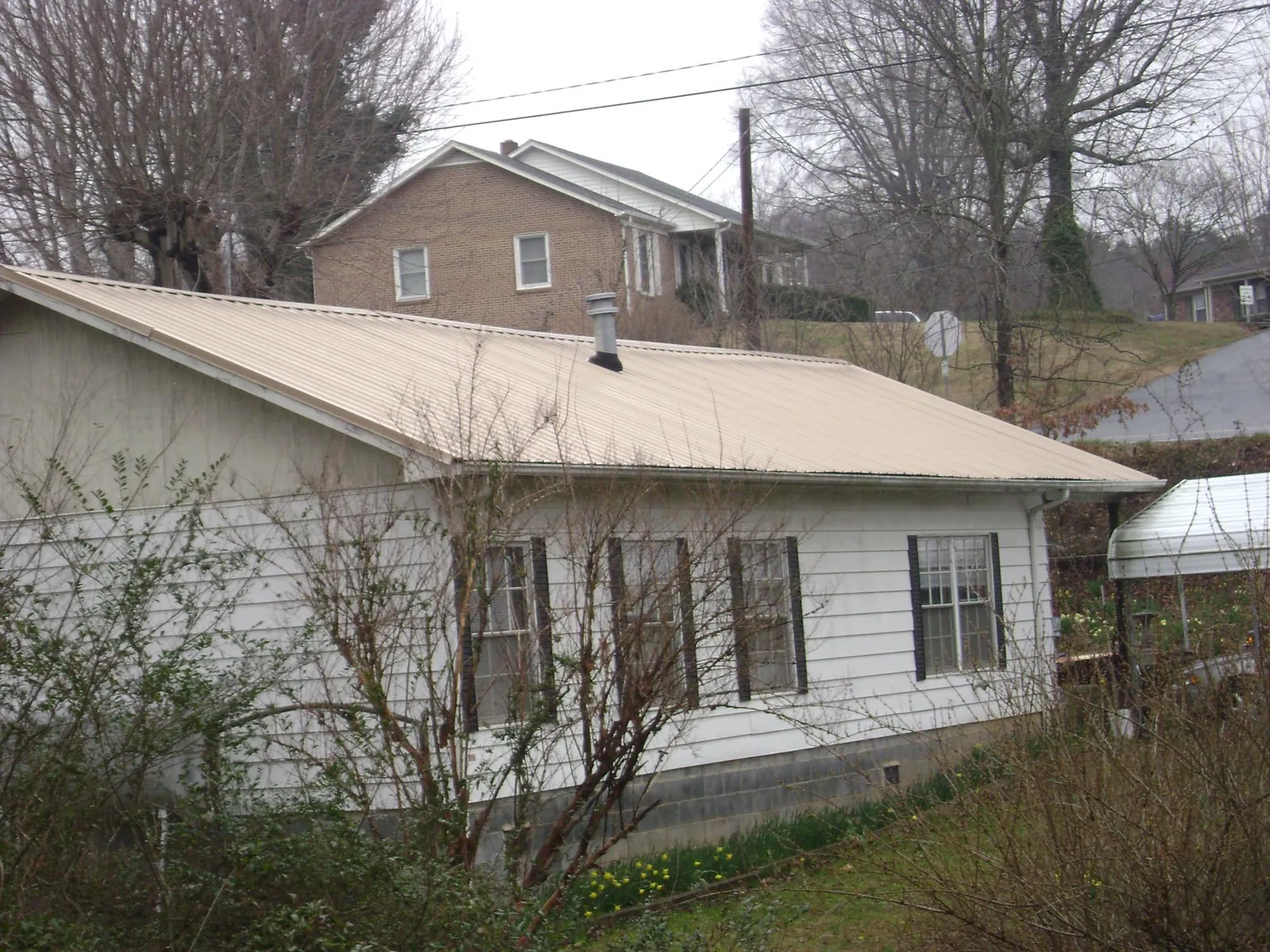 Tan metal roof on a white sided house set into a hillside — Commercial Roofing by Roofing Brothers in Newalla