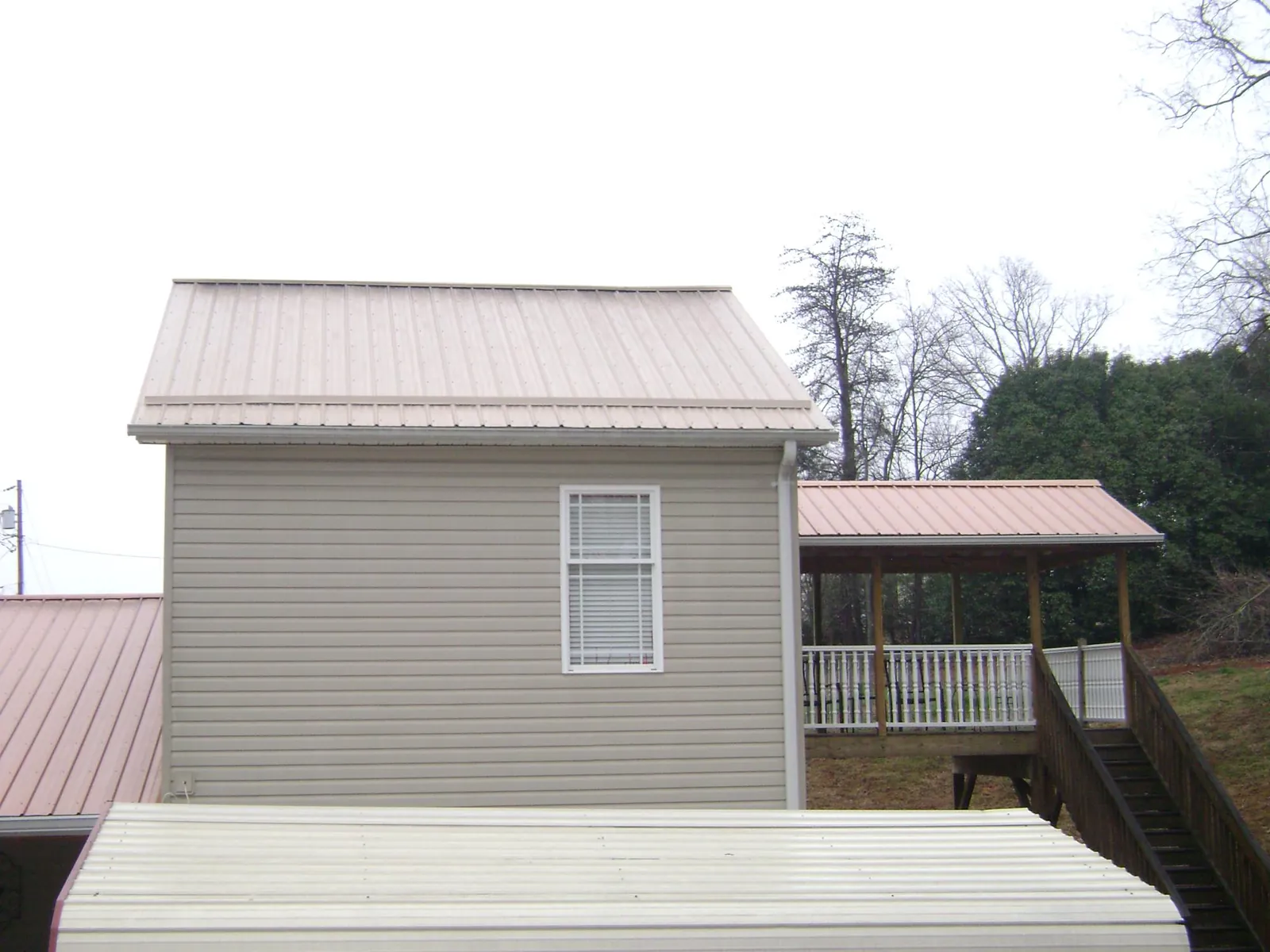 Tan metal roofs on a two story addition and attached porch, from a Roof Replacement job in Newalla